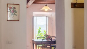 A dining area with a table and chairs, a hanging light fixture, and a view of greenery outside. - Tuscan Hilltop Getaway (Castelnuovo di Val di Cecina)
