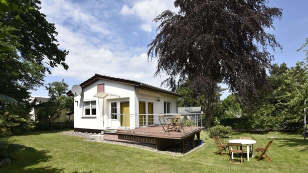 A single-story house with a deck, a small patio, and a lawn.