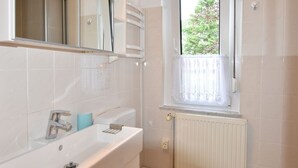 A bathroom with a white sink, mirror, and window with a white curtain.