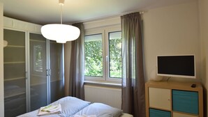 A bedroom with a bed, a wardrobe, a television, and a window with curtains.