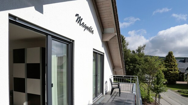 A building with a name sign 'Magnolia' and a balcony with a chair. - Serene Villa in Kstelberg near Lake & Watersports (Medebach)