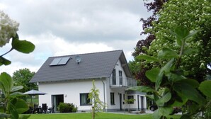 A two-story house with a sloped roof, satellite dish, and a small garden area with a lawn and a few trees. - Serene Villa in Kstelberg near Lake & Watersports (Medebach)