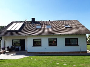 Una casa a due piani con tetto in tegole, un piccolo balcone e un patio lastricato con mobili da esterno.