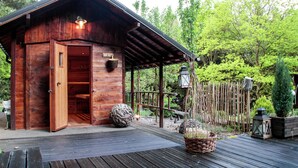 A wooden cabin with an open door, a wooden deck, and a garden with a wooden fence and trees. - Chalet Near Bitche With Private Sauna (Bousseviller)