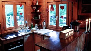 A wooden cabin kitchen with a sink, stove, and a window with heart decorations. - Chalet Near Bitche With Private Sauna (Bousseviller)