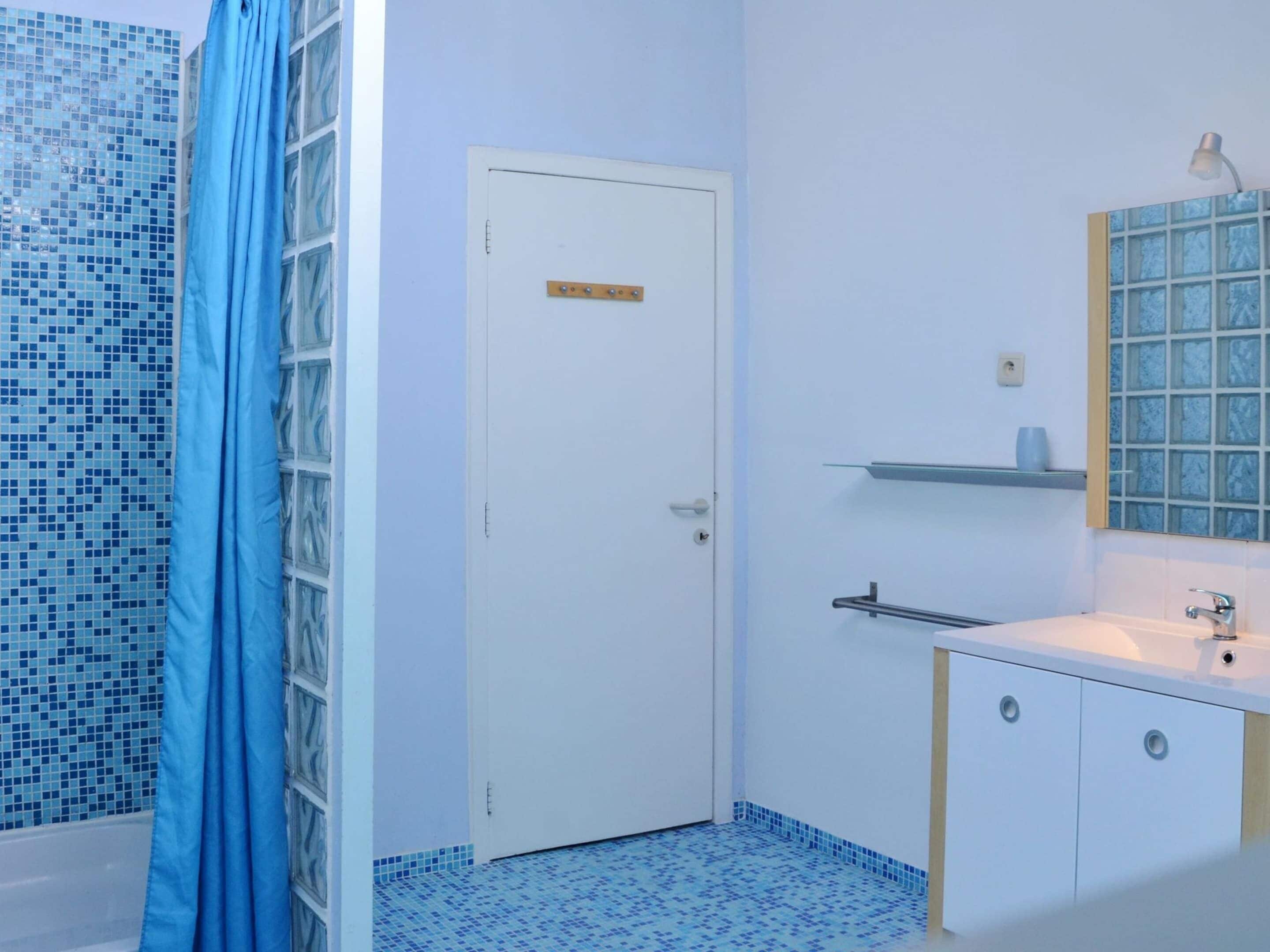 A bathroom with a white door, a sink with a mirror, and a shower area with blue tiles.
