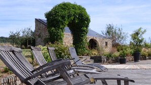 Outdoor wooden lounge chairs arranged on a wooden deck with a stone building and greenery in the background. - Charming Ardennes Getaway (Stoumont)