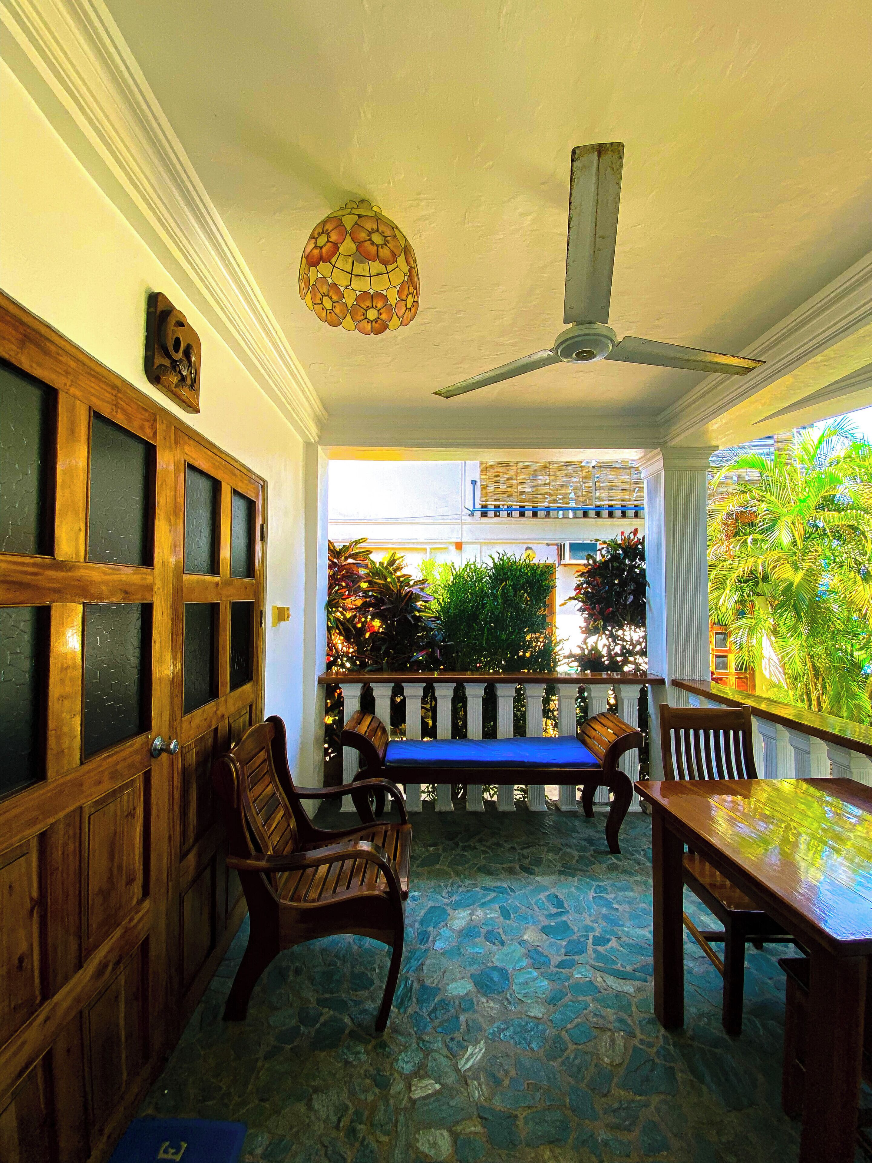 A covered patio with wooden furniture, a ceiling fan, and a decorative light fixture.