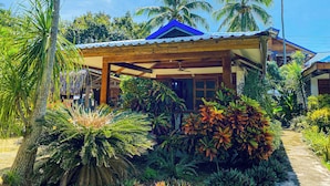 Ein Haus mit überdachter Veranda, umgeben von tropischer Vegetation und Palmen.