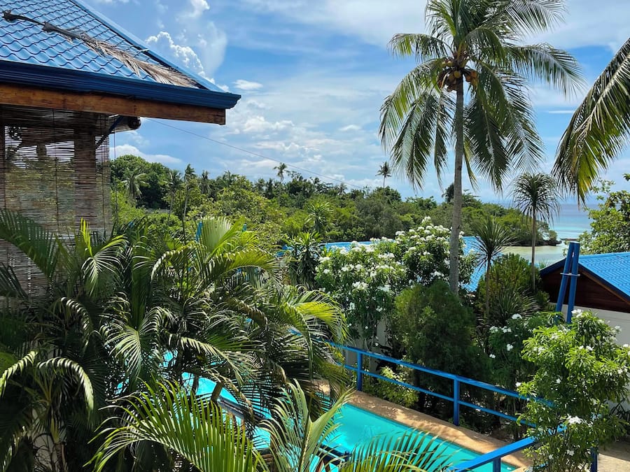 A pool area surrounded by lush greenery and palm trees, with a clear view of the ocean in the background.