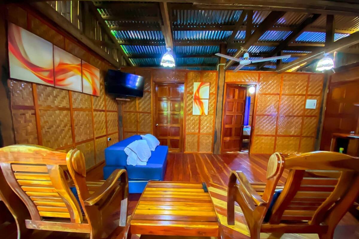 Une pièce avec un plancher en bois, un canapé bleu et des chaises en bois. Un téléviseur est fixé au mur.