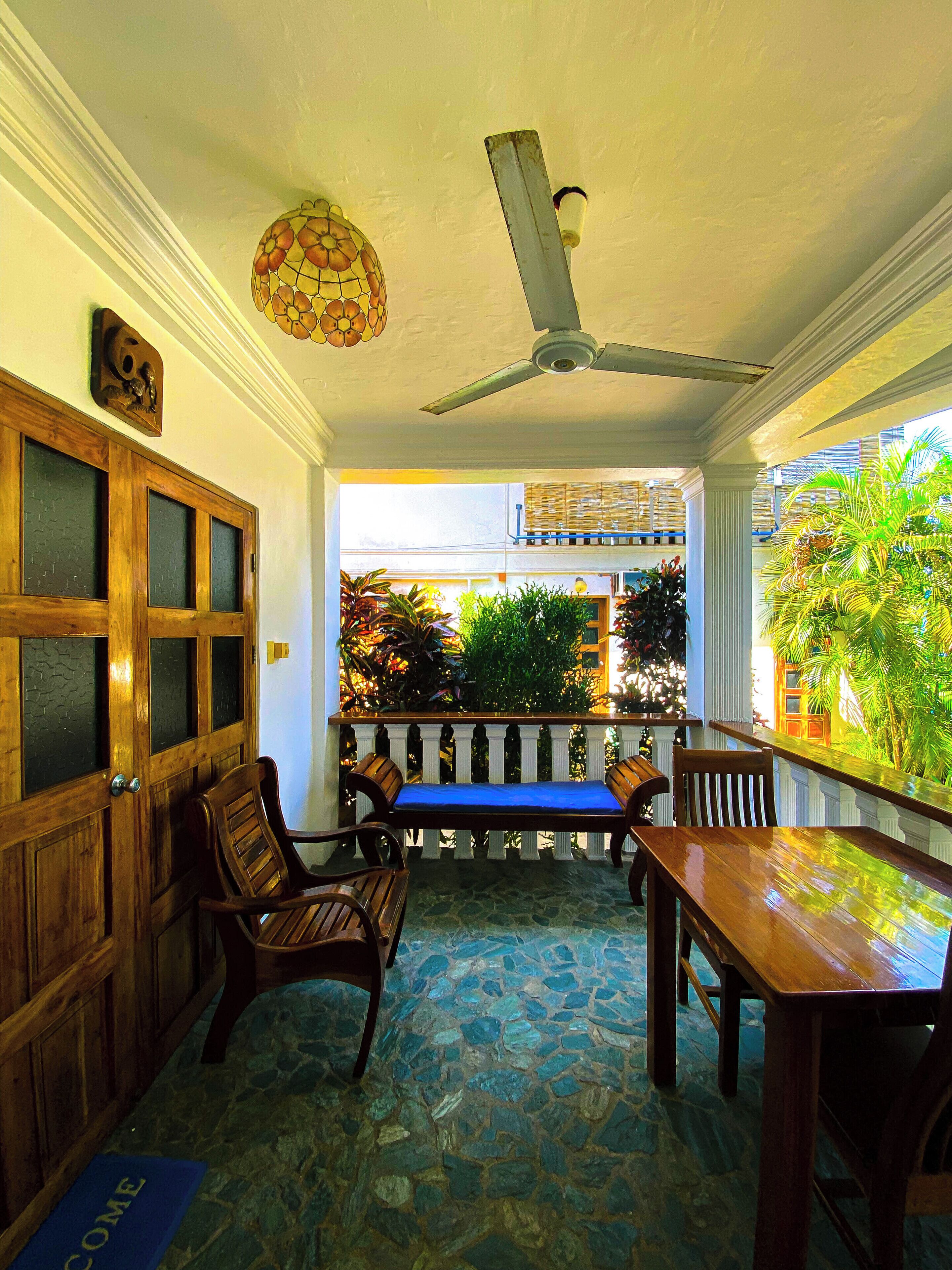 A covered outdoor seating area with stone flooring, wooden furniture, and a ceiling fan.