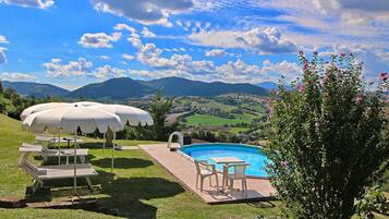 Relax by the serene pool surrounded by lush green hills and a garden with blooming flowers.