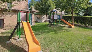 A playground with slides and climbing structures, surrounded by a grassy area and trees. - Apartment in Piticchio With Pool and BBQ (Arcevia)