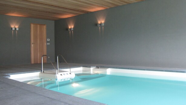 An indoor swimming pool with a wooden ceiling, a door, and wall-mounted lights. - Beernem Farmhouse With Pool (Beernem)