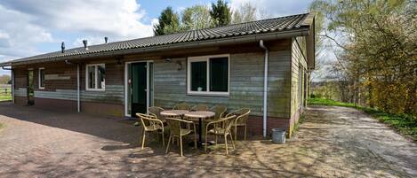 A single-story building with a tiled roof, a brick exterior, and a paved patio area with wicker furniture.