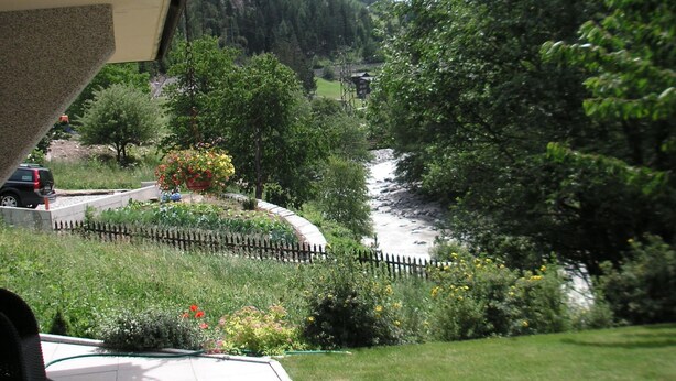 Ein Fluss fließt durch einen üppigen Garten mit einem Holzzaun und einem Berg im Hintergrund.