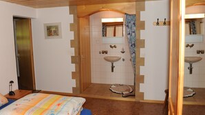 Ein Schlafzimmer mit Holzbalkendecke, einem Bett mit farbenfroher Steppdecke, einem Badezimmer mit Waschbecken und Spiegel sowie einer Tür zu einem anderen Raum.