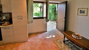 Una cocina con comedor, una ventana con cortinas, una puerta que da al exterior y piso de baldosas.