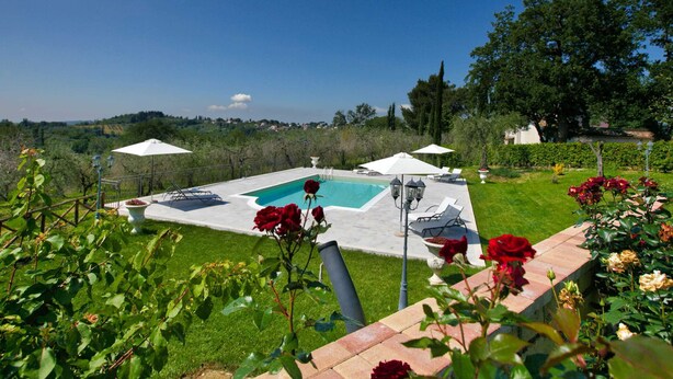 Una piscina rectangular con una vista despejada del paisaje circundante, incluyendo árboles y edificios al lejano.