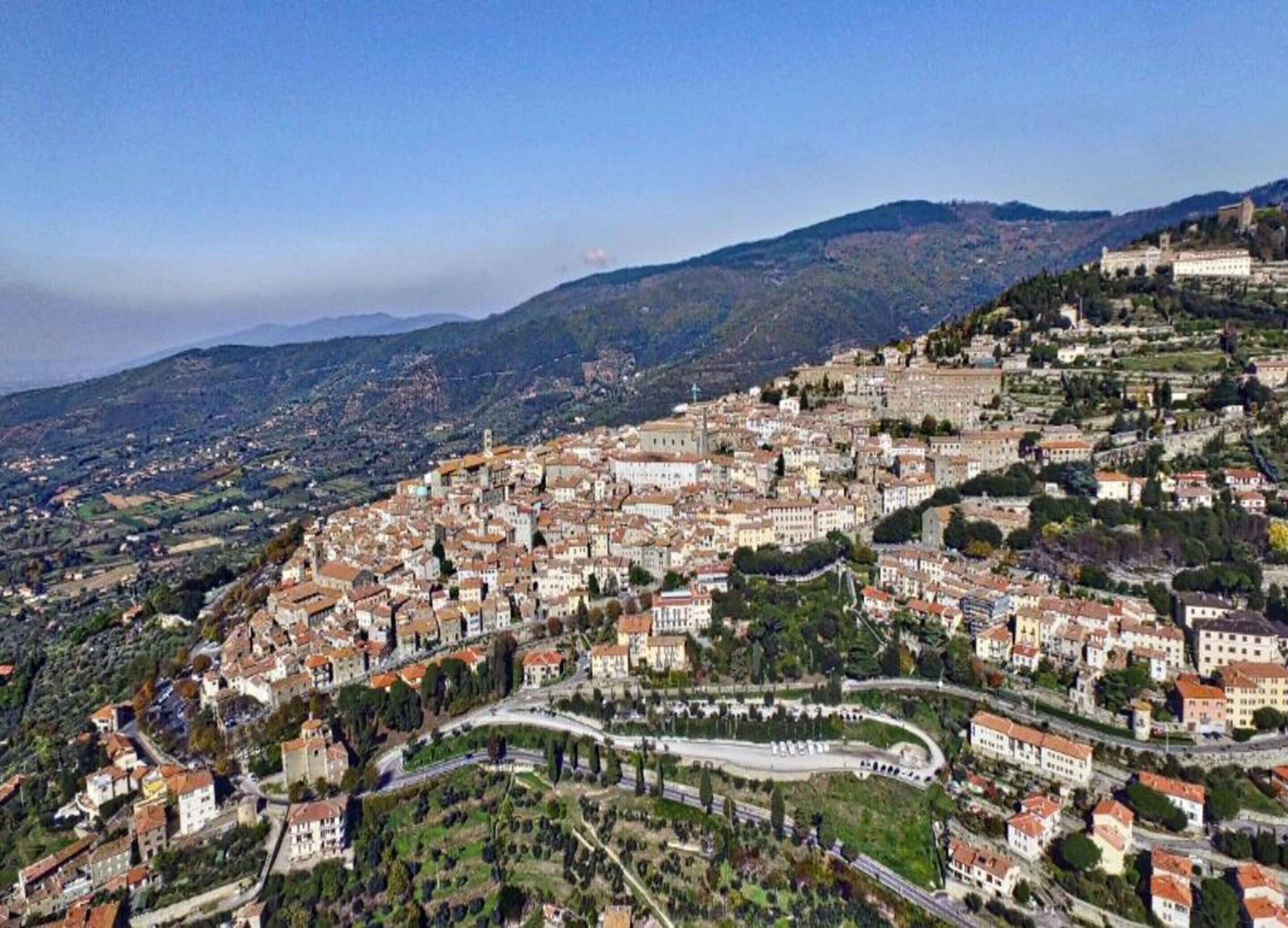 Vista panorâmica de uma cidade histórica, com um conjunto denso de edifícios, estradas sinuosas e uma estrutura imponente no topo da colina.