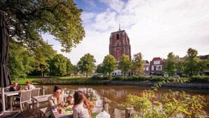 Un espace de restauration au bord de la rivière, avec des tables et des bancs en bois, offrant une vue sur un canal et une tour historique en arrière-plan.
