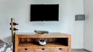A wooden cabinet with a television mounted above it, a small shelf with a cat figurine, and a wine rack to the left. - Holiday Home With Balcony (Bruck an der Grossglocknerstrasse)