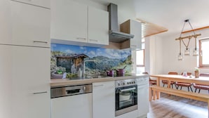 A modern kitchen with white cabinetry, a built-in oven, and a stove. There's a dining area with a wooden table and chairs. - Holiday Home With Balcony (Bruck an der Grossglocknerstrasse)
