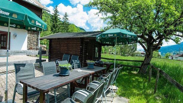 An outdoor dining area with a wooden table and metal chairs, surrounded by a stone wall and a wooden fence. - Holiday Home With Balcony (Bruck an der Grossglocknerstrasse)
