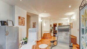 A modern hotel room with a large refrigerator, two lounge chairs, a small round table, and a shower area. - Apartment in Schleiden With Sauna and Nature (Hellenthal)
