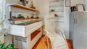 A kitchen with a white countertop, a sink, a chair, a refrigerator, and shelves with glassware and flowers. - Apartment in Schleiden With Sauna and Nature (Hellenthal)