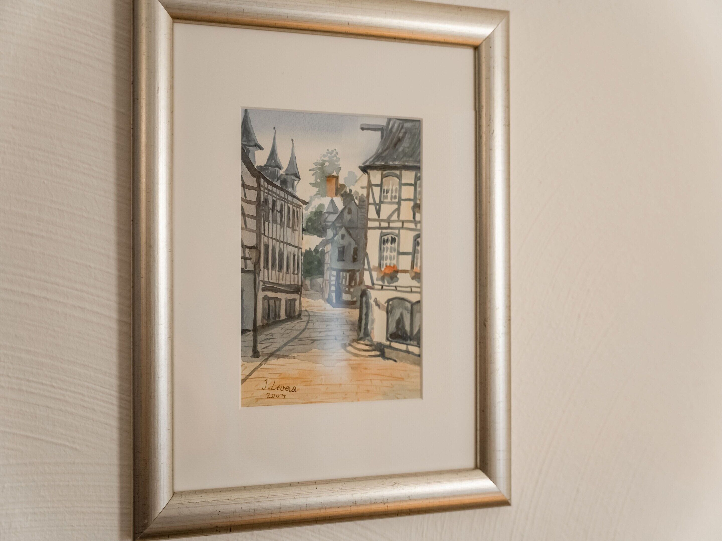 A framed watercolor painting of a narrow street with buildings on either side, signed by the artist in 2007.