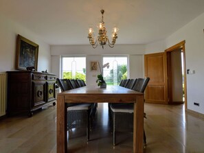 A dining area with a wooden table and wicker chairs, a chandelier, a radiator, and a door leading outside.