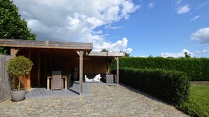 A covered outdoor patio area with stone flooring, wooden furniture, and a potted plant. - Spacious Villa in Zingem With Garden (Vresse-sur-Semois)