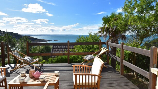 A wooden deck with two lounge chairs, a table with cups and a teapot, and a view of the sea. - Sea View Stay in Fermanville (Fermanville)
