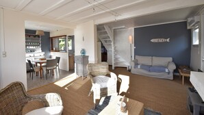 A spacious living area with a dining set, wicker furniture, a staircase, and a wall with a fish sign. - Sea View Stay in Fermanville (Fermanville)