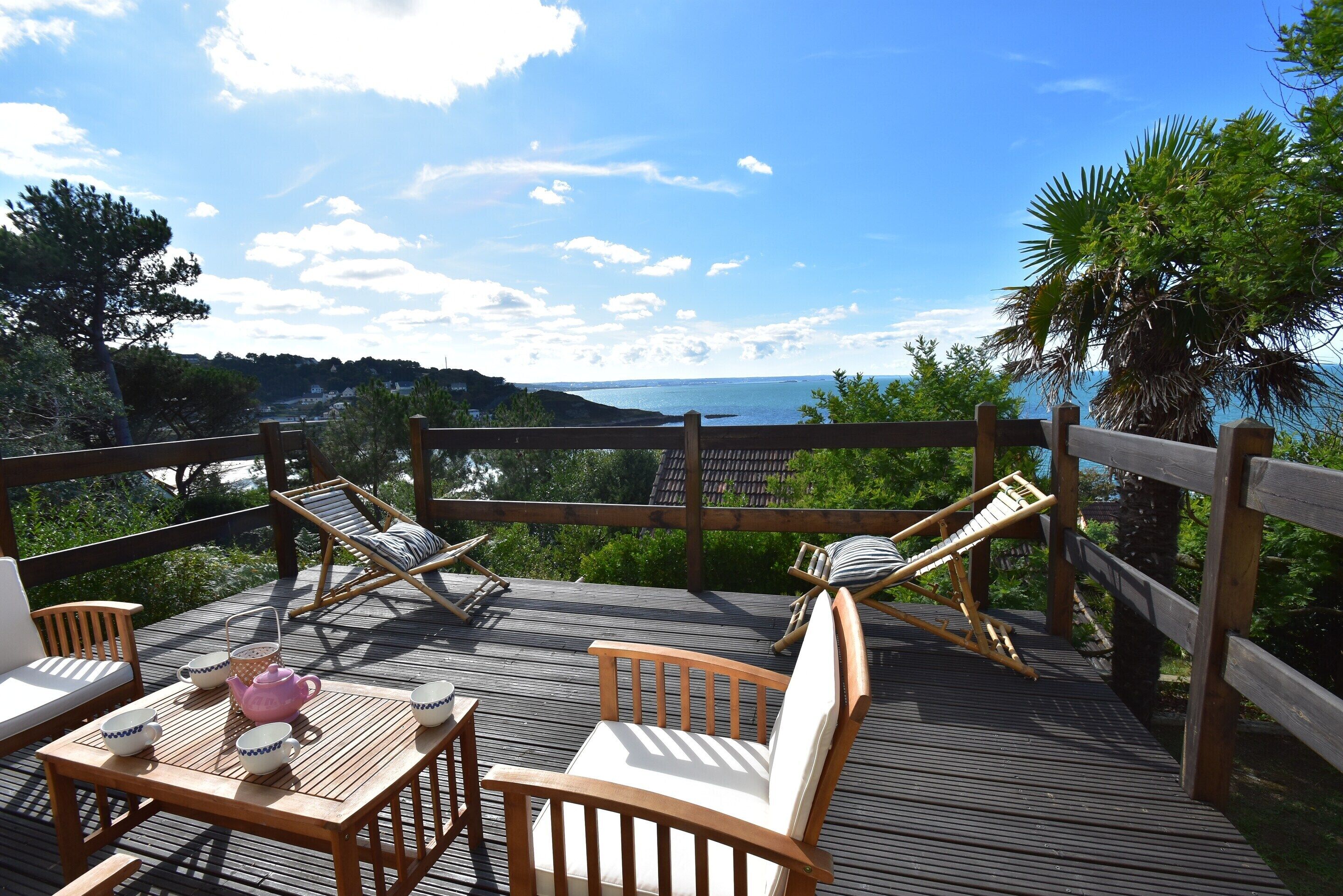A wooden deck with lounge chairs and a table, overlooking a body of water and greenery.