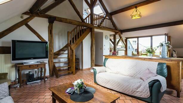 Un loft spacieux avec des poutres apparentes, un escalier en bois, une télévision, un canapé et un coin repas.