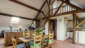 Une cuisine rustique avec des poutres en bois, un coin repas avec une table et des chaises en bois, et une vue sur l’espace de vie adjacent.