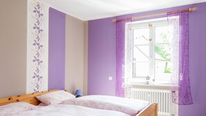 Une chambre avec deux lits, une fenêtre avec des rideaux violets et un radiateur.