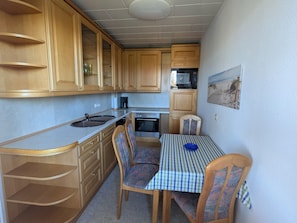 Une cuisine compacte dotée de meubles en bois, d’un four à micro-ondes, d’un four traditionnel et d’une table à manger avec des chaises.