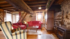 A rustic interior with a wooden ceiling, stone walls, a red sofa, a striped armchair, and a fireplace. - Gouvets Family Retreat (Gouvets)