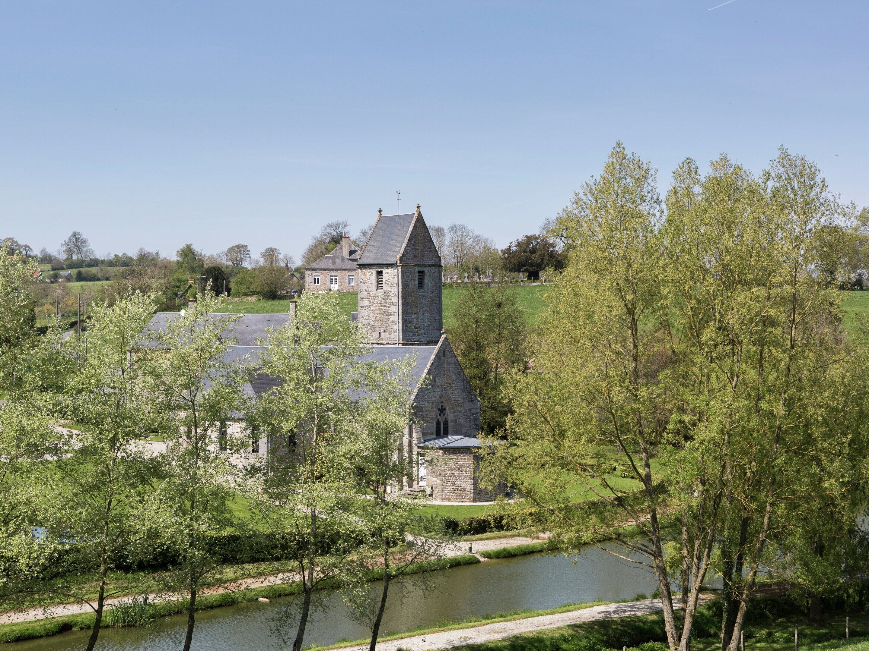 A stone church with a tower, surrounded by greenery and a river.