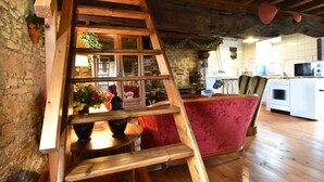 A wooden ladder leading to a lofted area with a red chair, kitchen appliances, and a stone wall. - Gouvets Family Retreat (Gouvets)