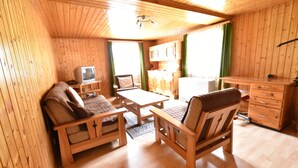 A wooden cabin interior with a sofa, two chairs, a small table, a television, and a kitchenette. - Cozy Stay Near Aletsch (Grengiols)