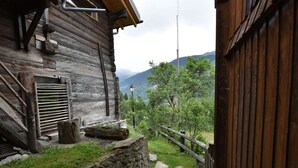 A rustic wooden cabin with a wooden staircase leading to a door, surrounded by a stone wall and a wooden fence. - Cozy Stay Near Aletsch (Grengiols)