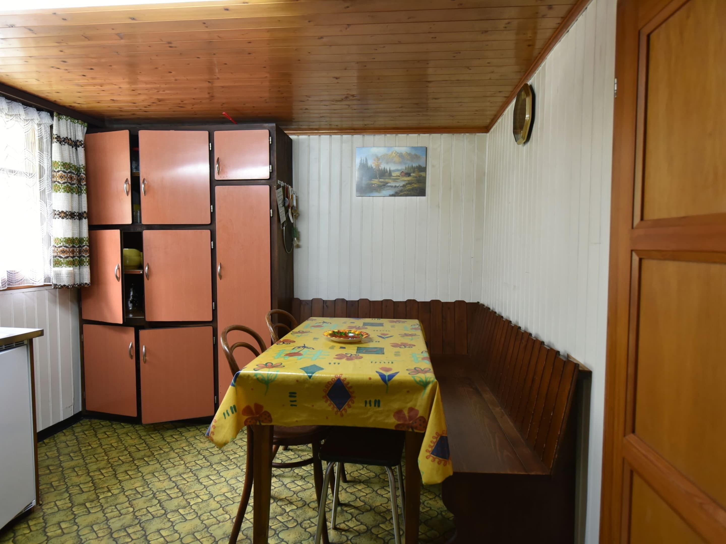 A compact kitchen with a wooden ceiling, a dining table with a yellow tablecloth, and a built-in bench.