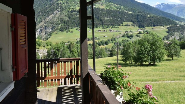 A wooden balcony with a view of a mountainous landscape, including a village and green fields. - Cozy Stay Near Aletsch (Grengiols)