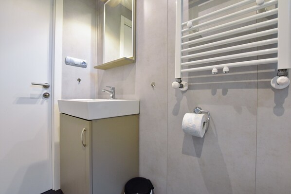 Un baño con lavamanos, espejo, toallero y dispensador de papel higiénico.