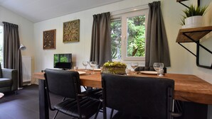 Un coin repas avec une table en bois, deux chaises noires, un téléviseur et une fenêtre avec des rideaux.